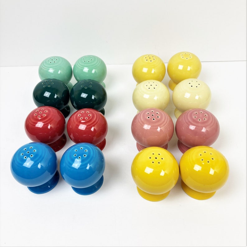 May include: Set of 12 colourful ceramic salt and pepper shakers. The shakers are round with a small hole on top for dispensing salt or pepper. The colours include green, blue, yellow, red, and pink.