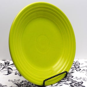 May include: A bright green ceramic dinner plate with a rippled design. The plate is on a black metal stand.