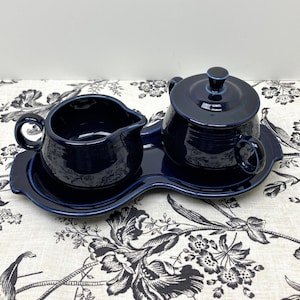 May include: A blue ceramic creamer and sugar bowl set with a matching tray. The set is in a deep blue color and has a simple, elegant design.