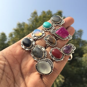 May include: A collection of nine silver rings featuring different coloured gemstones. The rings have intricate designs and are set with various stones, including turquoise, amethyst, and labradorite.