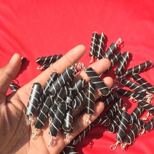 Puede incluir: Un mont&oacute;n de colgantes envueltos en alambre negro y plateado. Los colgantes tienen forma de peque&ntilde;os cilindros y tienen un bucle plateado en la parte superior.