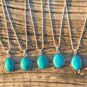 Könnte beinhalten: Fünf silberne Halsketten mit ovalen Türkis-Anhängern. Die Halsketten liegen auf einer Holzoberfläche.
