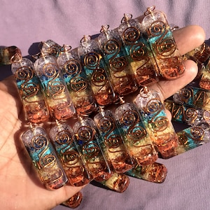 Pu&ograve; includere: Una collezione di ciondoli di cristallo dei sette chakra con filo di rame avvolto attorno. Ogni ciondolo &egrave; fatto di quarzo trasparente con sette strati di cristalli di diversi colori che rappresentano i sette chakra. I ciondoli sono disposti in una mano, con la parte superiore dei ciondoli rivolta verso lo spettatore.