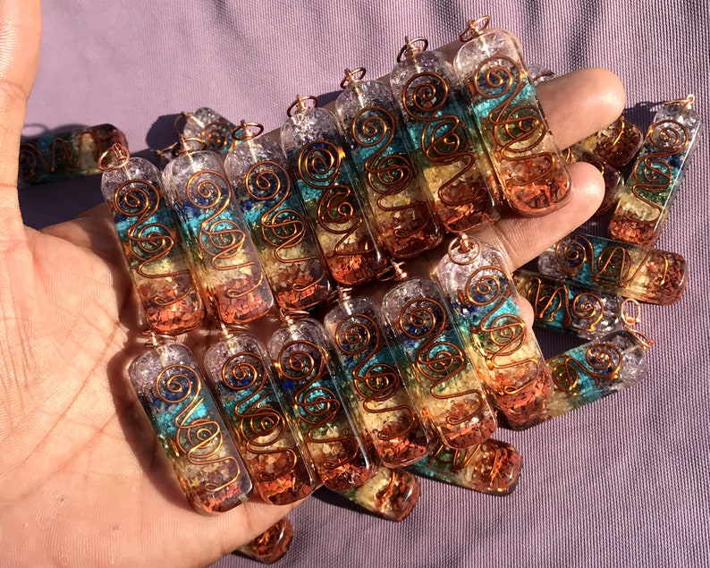 Pu&ograve; includere: Una collezione di ciondoli di cristallo dei sette chakra con filo di rame avvolto attorno. Ogni ciondolo &egrave; fatto di quarzo trasparente con sette strati di cristalli di diversi colori che rappresentano i sette chakra. I ciondoli sono disposti in una mano, con la parte superiore dei ciondoli rivolta verso lo spettatore.