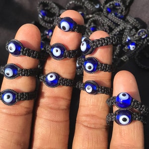 May include: A set of black string bracelets with blue evil eye charms. The bracelets are adjustable and can be worn on the wrist or ankle.