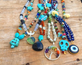 Può includere: Sette collane di perline colorate con vari ciondoli, tra cui un teschio turchese, un cuore verde, una pietra nera, un albero della vita e un occhio turco blu. Le collane sono realizzate con diversi materiali, come roccia lavica, turchese e perline di vetro.