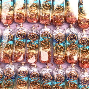 Pu&ograve; includere: Una collezione di sette bacchette di cristallo del chakra con filo di rame avvolto attorno. Le bacchette sono riempite con cristalli di quarzo trasparente e pietre di vari colori, che rappresentano i sette chakra. Le bacchette sono disposte in una fila su una superficie viola.