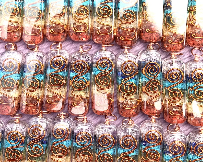 Pu&ograve; includere: Una collezione di sette bacchette di cristallo del chakra con filo di rame avvolto attorno. Le bacchette sono riempite con cristalli di quarzo trasparente e pietre di vari colori, che rappresentano i sette chakra. Le bacchette sono disposte in una fila su una superficie viola.