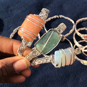 Op de afbeelding: Drie zilveren draadgewikkelde armbanden met verschillende gekleurde stenen. De armbanden hebben een lichtoranje steen, een groene steen en een witte steen.