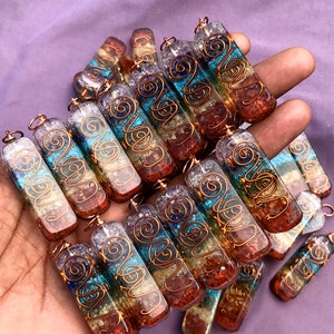 Pu&ograve; includere: Una collezione di sette ciondoli di cristallo dei sette chakra, ognuno con un filo di rame avvolto attorno. I ciondoli sono in quarzo trasparente con sette pietre di colori diversi incastonate, che rappresentano i sette chakra. I ciondoli sono disposti in una pila, con il filo di rame visibile su ognuno.