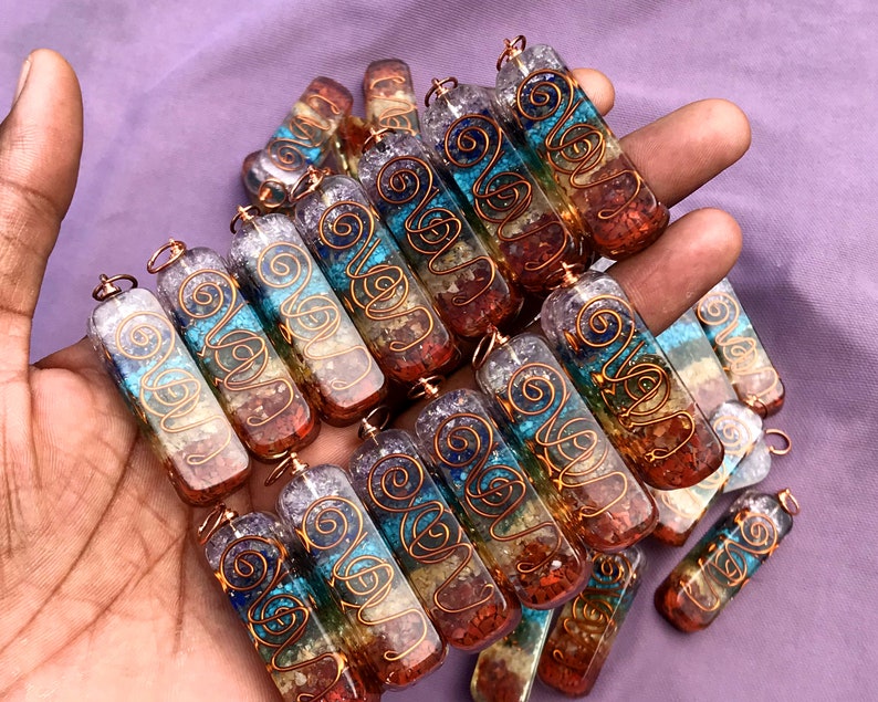 Pu&ograve; includere: Una collezione di sette ciondoli di cristallo dei sette chakra, ognuno con un filo di rame avvolto attorno. I ciondoli sono in quarzo trasparente con sette pietre di colori diversi incastonate, che rappresentano i sette chakra. I ciondoli sono disposti in una pila, con il filo di rame visibile su ognuno.