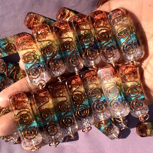 Pu&ograve; includere: Primo piano di un mucchio di bacchette di cristallo dei sette chakra con filo di rame avvolto attorno. Le bacchette sono in quarzo trasparente con cristalli di diversi colori incastonati, che rappresentano i sette chakra. Le bacchette sono lunghe circa 5 cm.