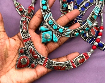Può includere: Una collana d'argento con pietre rosse e turchesi. La collana è realizzata con un'intricata lavorazione in argento e presenta una varietà di forme e dimensioni di pietre.