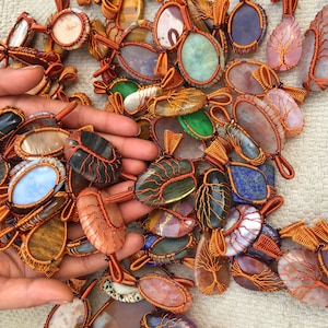 以下が含まれることがあります： さまざまな色と形をしたワイヤーで包まれた宝石のペンダントのコレクション。ペンダントは銅線で作られており、瑪瑙、アメジスト、水晶など、さまざまな石が特徴です。