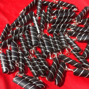 Puede incluir: Un grupo de colgantes de obsidiana negra envueltos en alambre de plata. Los colgantes son todos del mismo tama&ntilde;o y forma, y est&aacute;n dispuestos en una pila sobre una superficie roja.