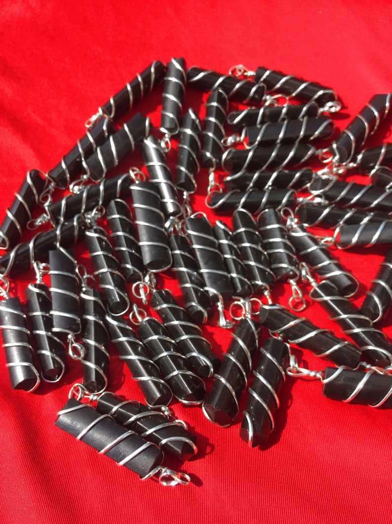Puede incluir: Un grupo de colgantes de obsidiana negra envueltos en alambre de plata. Los colgantes son todos del mismo tama&ntilde;o y forma, y est&aacute;n dispuestos en una pila sobre una superficie roja.