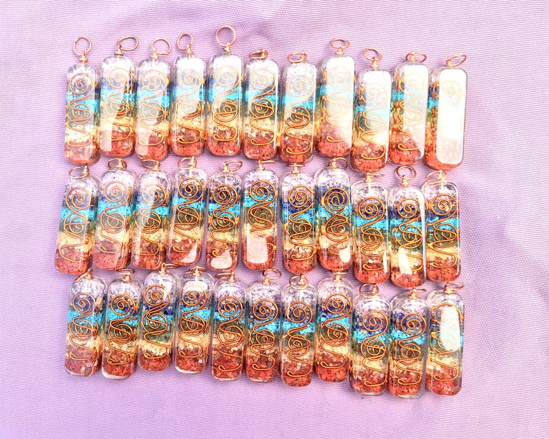 Pu&ograve; includere: Una collezione di 30 ciondoli in vetro trasparente con filo di rame avvolto attorno a pietre colorate all'interno. Le pietre sono disposte in un motivo arcobaleno, con pietre rosse, arancioni, gialle, verdi, blu e viola. I ciondoli sono tutti della stessa dimensione e forma, e sono disposti in uno schema a griglia.