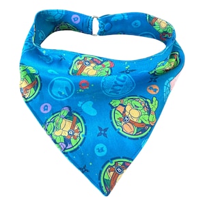 May include: A blue bandana with a Teenage Mutant Ninja Turtles pattern. The bandana features images of the four turtles, their names, and the iconic ninja stars.