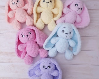 Könnte beinhalten: Sechs gehäkelte Hasen-Plüschtiere in verschiedenen Pastellfarben, darunter Rosa, Gelb, Hellblau und Lavendel. Jeder Hase hat lange, schlaffe Ohren und einen süßen Ausdruck.