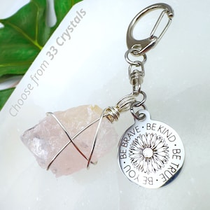 May include: A silver keychain with a pink crystal wrapped in wire and a silver charm with the words "Be You. Be Brave. Be Kind. Be True." and a flower design.