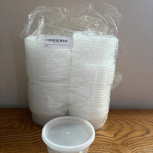 May include: A stack of clear plastic storage containers with lids, enclosed in a transparent plastic bag. A single container with a lid sits in front. A white label on the bag displays a barcode and the text Green Direct Plastic Storage.