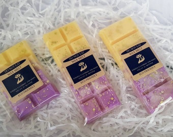 May include: Three wax melt bars in clear packaging, presented on a bed of white paper. The top half of each bar is yellow, transitioning to purple with gold flecks. Each package has a label that reads "DO NOT EAT WAX MELT" and "ECO FRIENDLY."