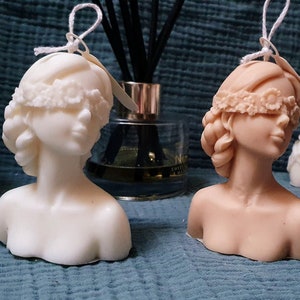 May include: Two handmade bust candles, one white and one beige, with blindfolds made of lace. Both candles have a tag that says "handmade with love".