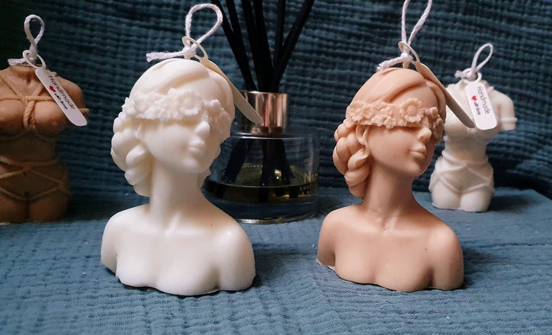 May include: Two handmade bust candles, one white and one beige, with blindfolds made of lace. Both candles have a tag that says "handmade with love".