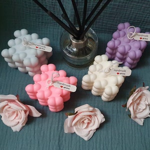 May include: Four handmade bubble candles in different colors: light blue, pink, white, and purple. Each candle has a small tag that says "Handmade with love".