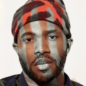 May include: A man with a beard wearing a camouflage beanie with orange accents. His face is painted with vertical stripes of silver and black.