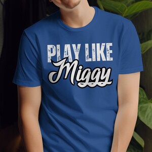 May include: A royal blue t-shirt with a white distressed graphic that reads "Play Like Miggy".