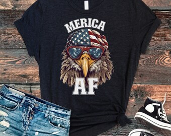 Peut inclure: Un t-shirt noir avec un graphique d'un aigle portant des lunettes de soleil et un bandana avec le drapeau américain. Le texte "Merica AF" est imprimé sous l'aigle.