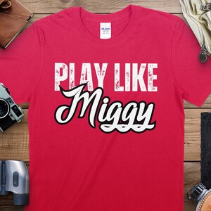 May include: Red t-shirt with white text that reads "Play Like Miggy".