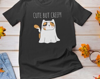 May include: Black t-shirt with a cute cartoon of a calico cat wearing a ghost costume. The text "Cute But Creepy" is printed above the cat.