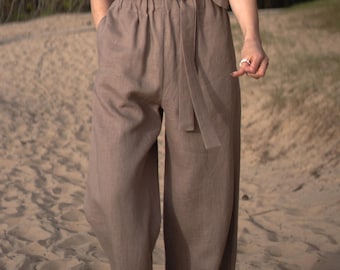 May include: A neutral brown linen two-piece outfit. The outfit comprises wide-leg trousers with an elasticated waistband and a matching wrap top with a tie fastening. The ensemble is made of a lightweight fabric, suitable for warmer weather.