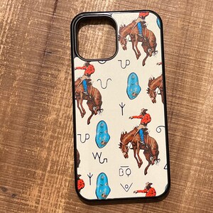 May include: A black phone case with a white background and a pattern of cowboys riding horses, turquoise stones, and Western symbols. The symbols include "UP", "W5", "BQ", and a horseshoe.