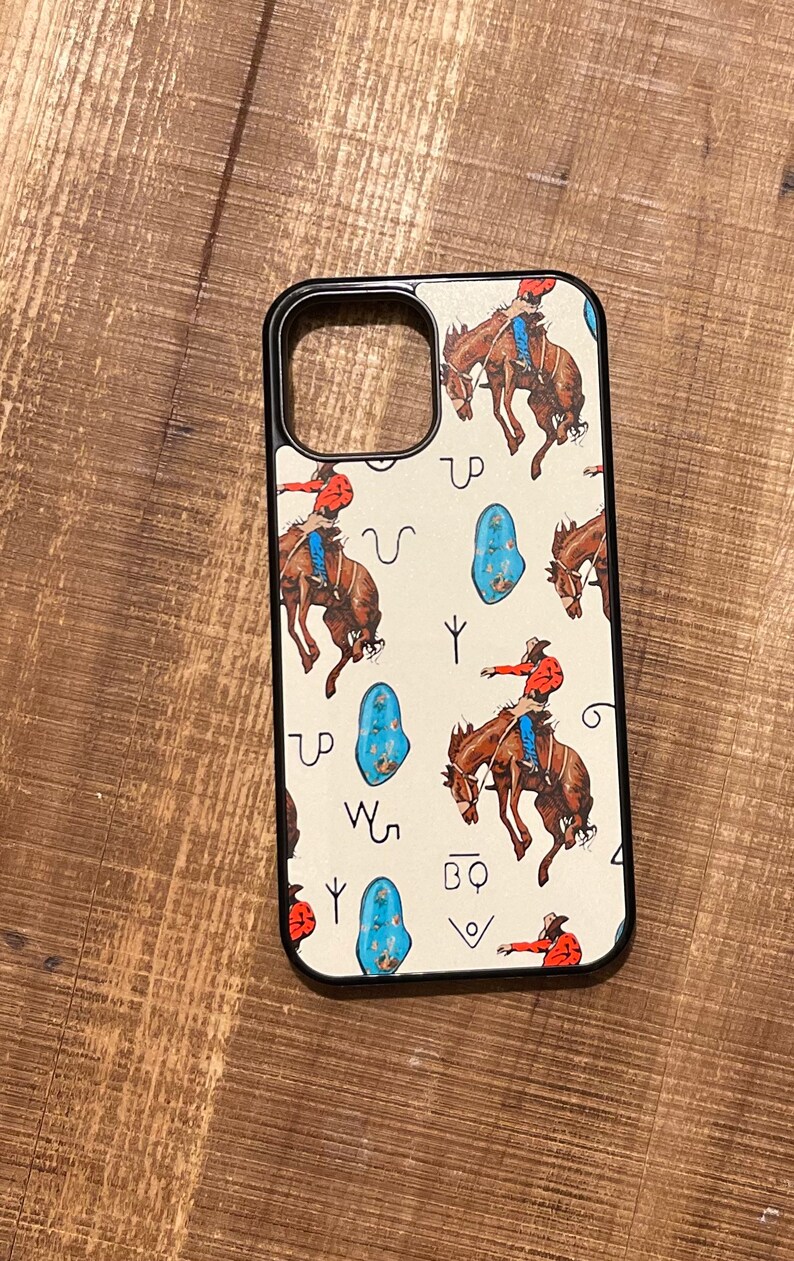 May include: A black phone case with a white background and a pattern of cowboys riding horses, turquoise stones, and Western symbols. The symbols include "UP", "W5", "BQ", and a horseshoe.
