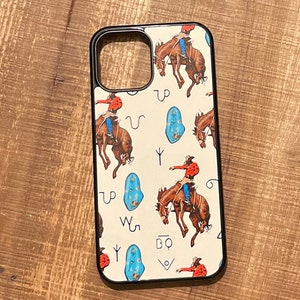 May include: A white phone case with a black border and a pattern of cowboys riding horses and turquoise stones. The case has a cutout for the camera lens and a black button on the side.