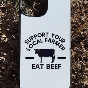 May include: White phone case with a black border and a black silhouette of a cow. The text on the case reads "Support Your Local Farmer - Eat Beef".