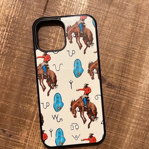 May include: A white phone case with a black border. The case features a pattern of cowboys riding horses, turquoise stones, and Western symbols. The symbols include a horseshoe, a lasso, and a branding iron.
