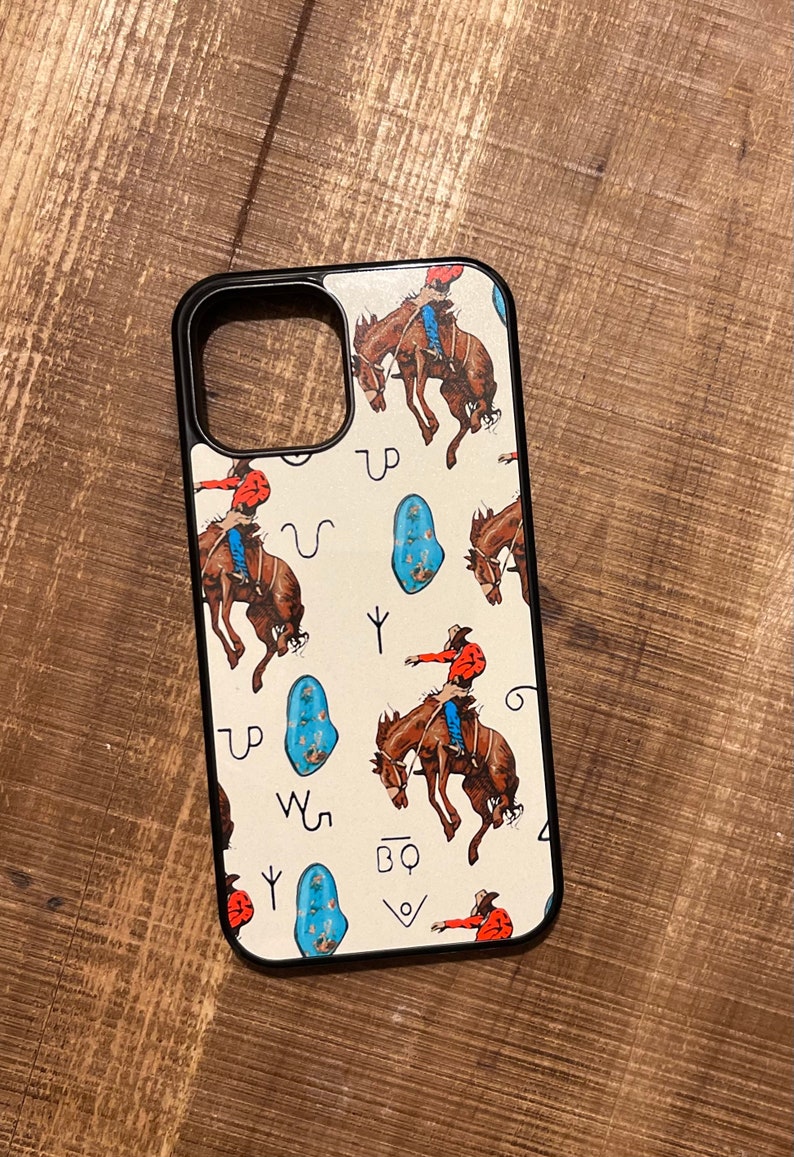 May include: A white phone case with a black border. The case features a pattern of cowboys riding horses, turquoise stones, and Western symbols. The symbols include a horseshoe, a lasso, and a branding iron.