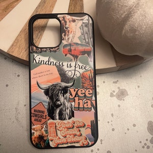 May include: A black phone case with a collage of colorful stickers. The stickers feature a cow, a cactus, a sunset, and the text "Kindness is free", "yee haw", and "Livin' the small town dream".