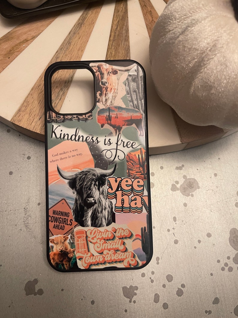 May include: A black phone case with a collage of colorful stickers. The stickers feature a cow, a cactus, a sunset, and the text "Kindness is free", "yee haw", and "Livin' the small town dream".