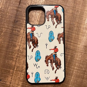 May include: A white phone case with a black border and a pattern of cowboys riding horses and turquoise stones. The case has the letters "BQ" and other symbols on it.