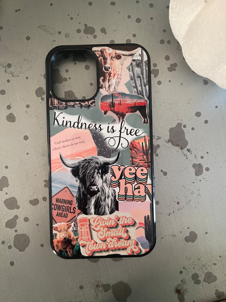 May include: A black phone case with a collage of colorful stickers. The stickers feature a cow, a cactus, a sunset, and the text "Kindness is free", "yee hay", and "Livin' the small town dream".