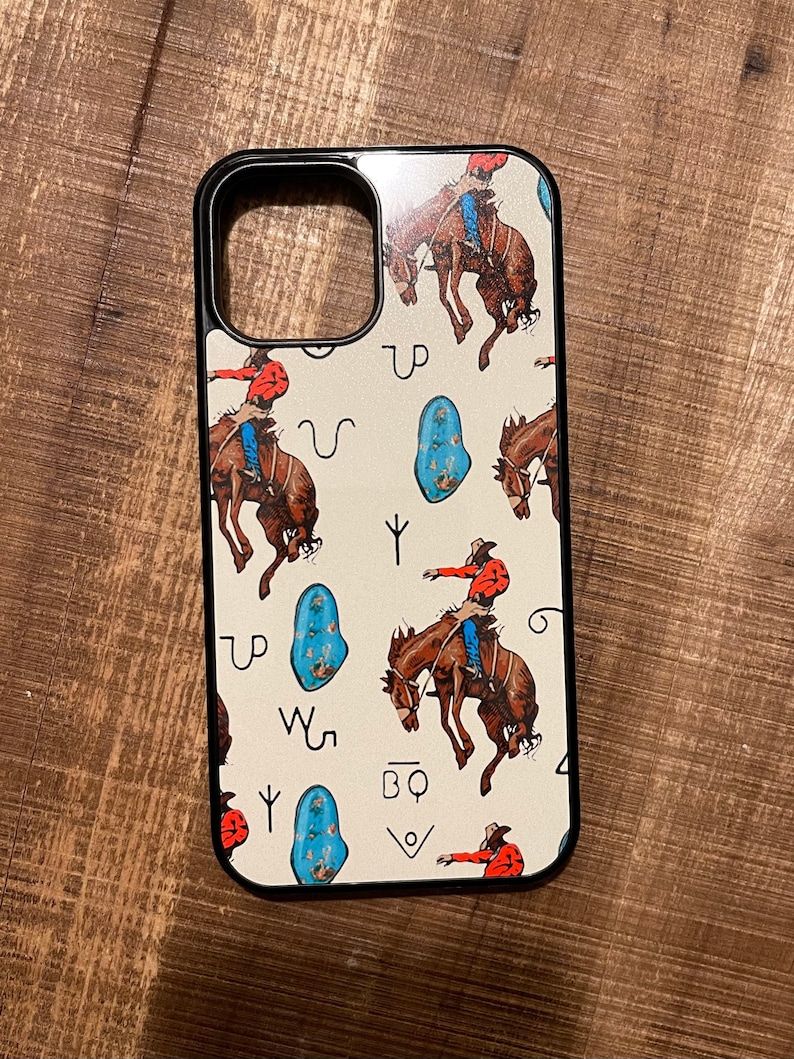 May include: A white phone case with a black border and a pattern of cowboys riding horses, turquoise stones, and symbols. The symbols include "UP", "W", "Y", and "BQ".