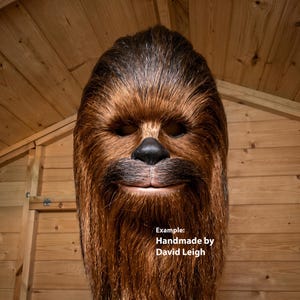 Pode incluir: Uma máscara de cabeça inteira de pelo castanho que se assemelha a um Wookiee, com pelo longo e desgrenhado, um nariz preto e aberturas para os olhos. O texto "Example: Handmade by David Leigh" está impresso a branco no lado inferior direito.