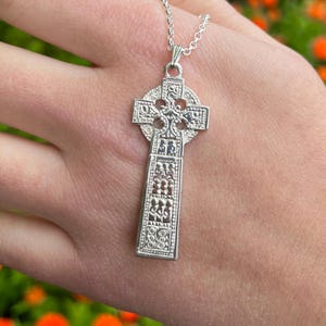 May include: A silver Celtic cross pendant with intricate knotwork designs. The cross is on a silver chain.
