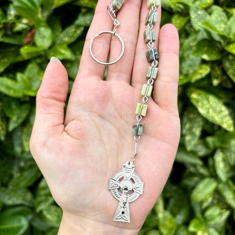 Pu&ograve; includere: Un portachiavi con un rosario di pietre verdi e bianche e un ciondolo a forma di croce celtica argentata. Il rosario &egrave; composto da piccole pietre quadrate.