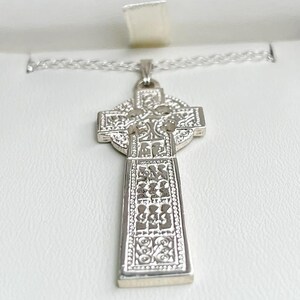 May include: A silver Celtic cross pendant necklace with intricate knotwork designs. The cross is detailed with a Celtic knot pattern and is suspended from a silver chain.